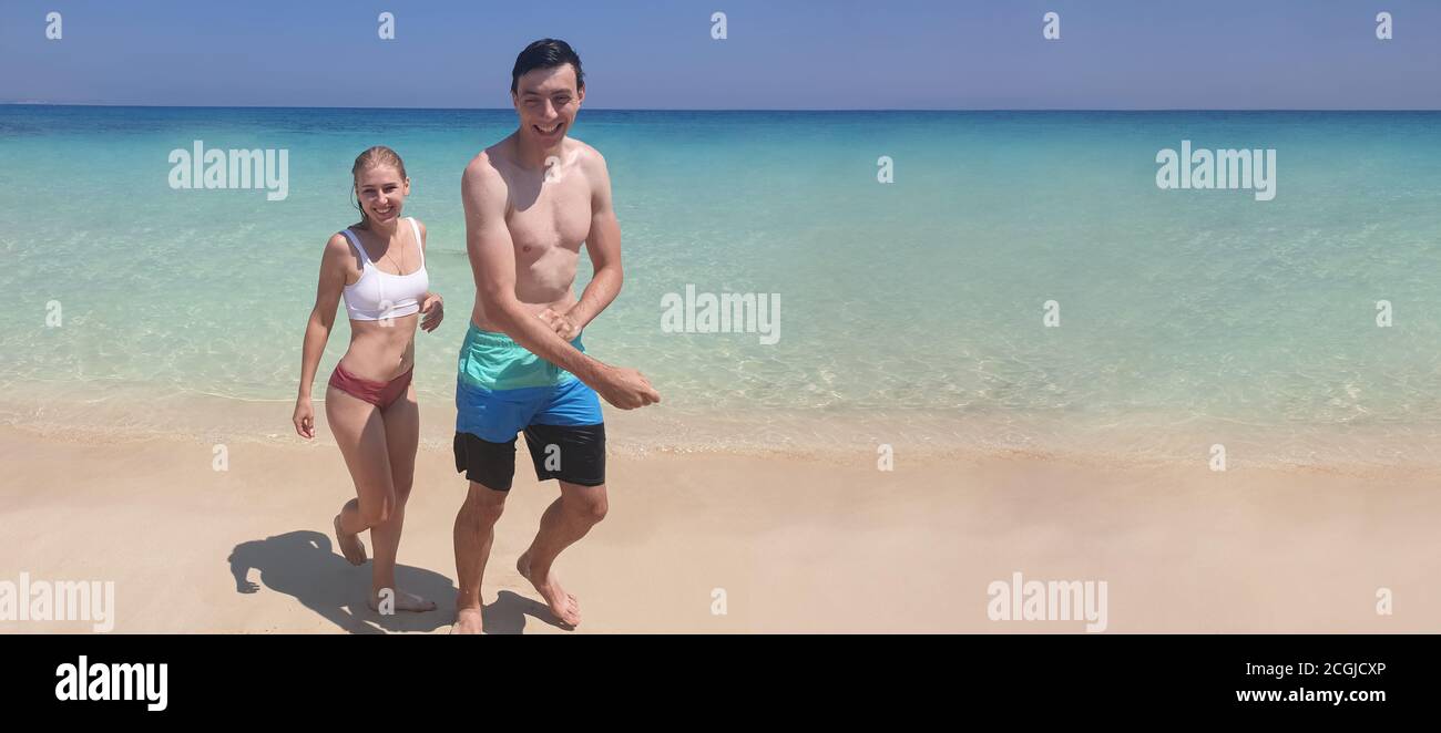 Vista panoramica di una coppia romantica sorridente uomo e donna in vacanza camminando su una spiaggia tropicale deserta con un banner web panoramico cielo blu chiaro. Foto Stock