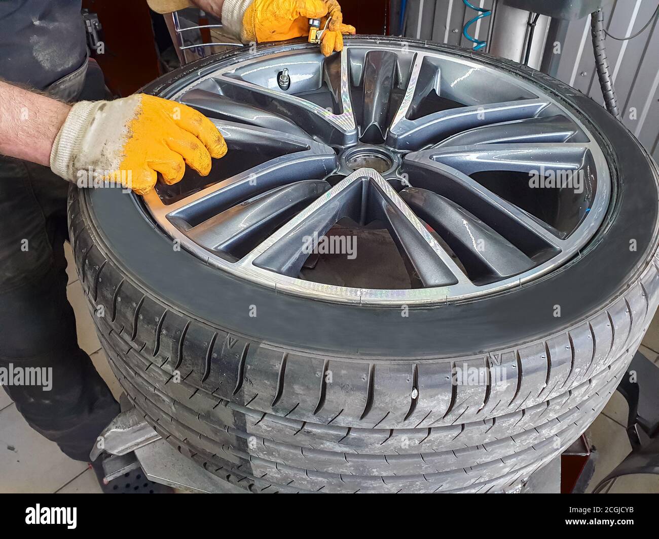 Servizio pneumatici stagionale. Meccanico professionista in un servizio di automobile. Una ruota per auto su una macchina per la sostituzione di pneumatici. Un meccanico al lavoro. Foto Stock
