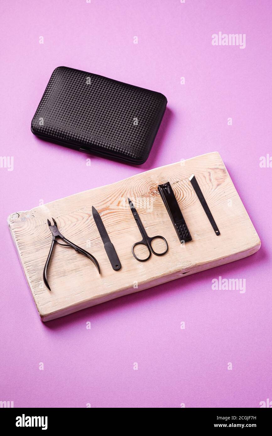 Set di utensili e accessori per manicure e pedicure su tavola di legno vicino al contenitore nero, vista angolare, sfondo rosa Foto Stock