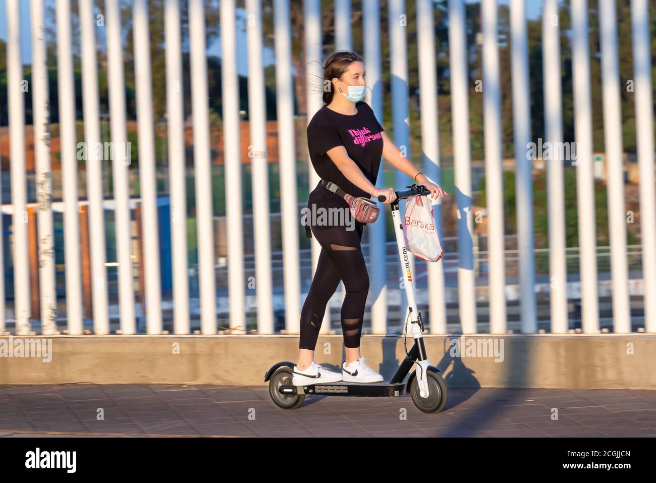 Huelva, Spagna - 10 settembre 2020: Giovane donna che cavalca uno scooter elettrico sul marciapiede indossando una maschera protettiva a causa del coronavirus covid-19 Foto Stock