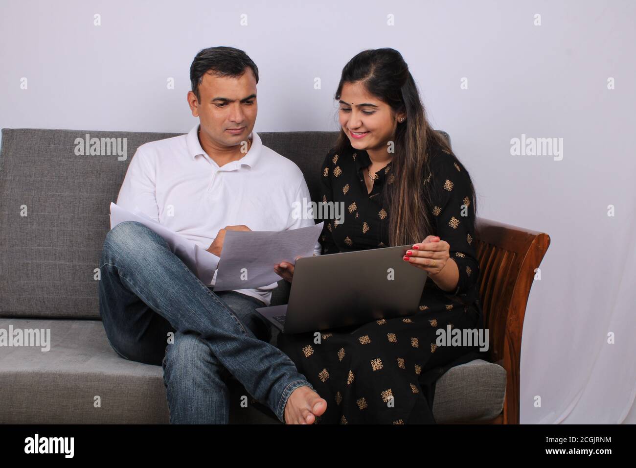 Concetto di persone, denaro e finanze. Giovane donna indiana seduta accanto al marito sul divano, lavorando con documenti e laptop. Foto Stock