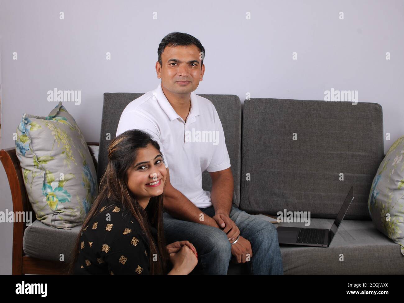 Giovane coppia indiana che usa il computer portatile seduto su un divano. Foto Stock