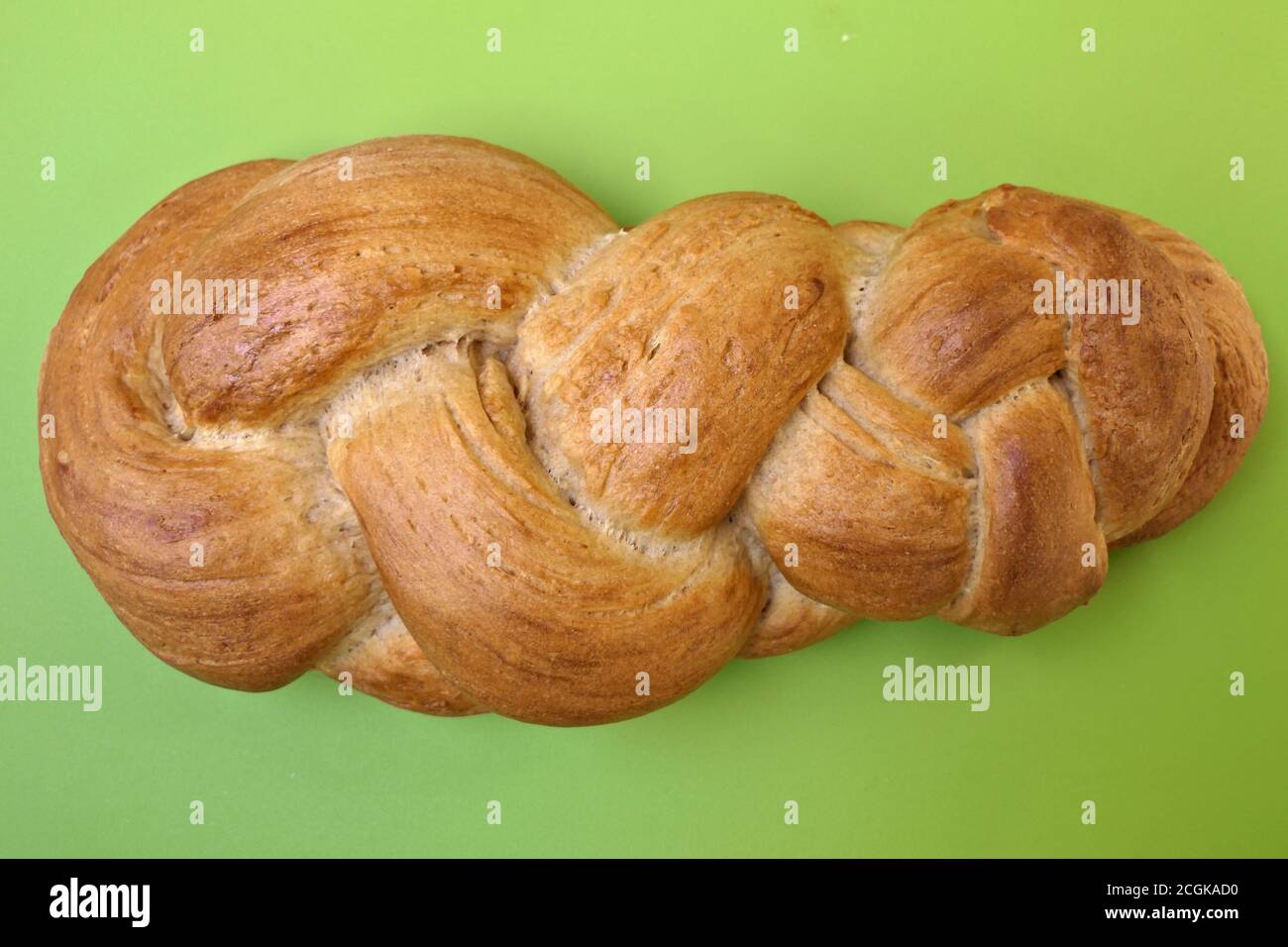 Primo piano treccia fresca fatta in casa o pane intrecciato dall'alto una tavola da carving verde pronta per una colazione domenicale al mattino Foto Stock