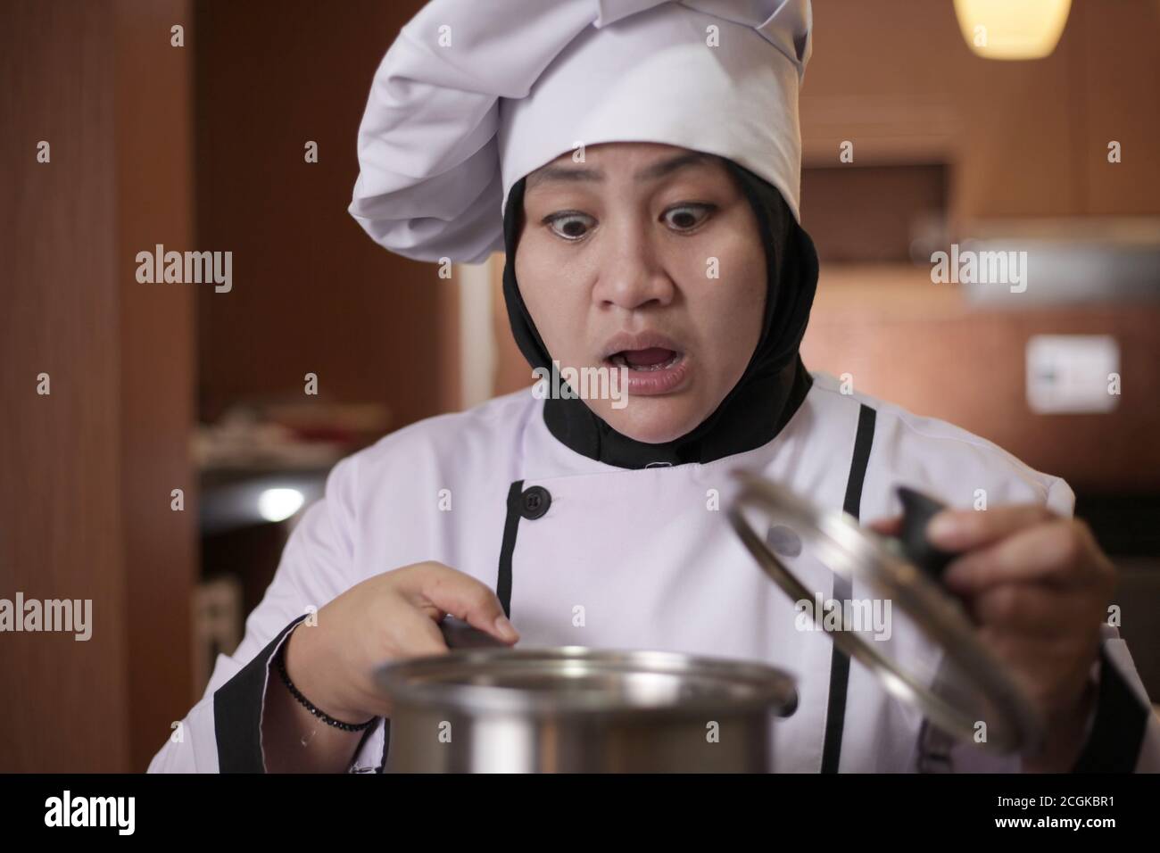 Cuoco asiatico femmina aprire pentola di cottura e odore di aroma di cibo che ha cucinato, fallimento nel concetto di cottura, male preoccupato espressione del viso Foto Stock