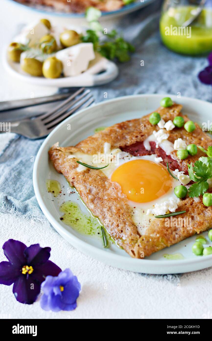 Il bretone tradizionale pancake fatti da farina di grano saraceno con prosciutto, formaggio, uovo, il formaggio feta, piselli verdi e burro verde. La prima colazione di grano saraceno frittelle sottili wi Foto Stock