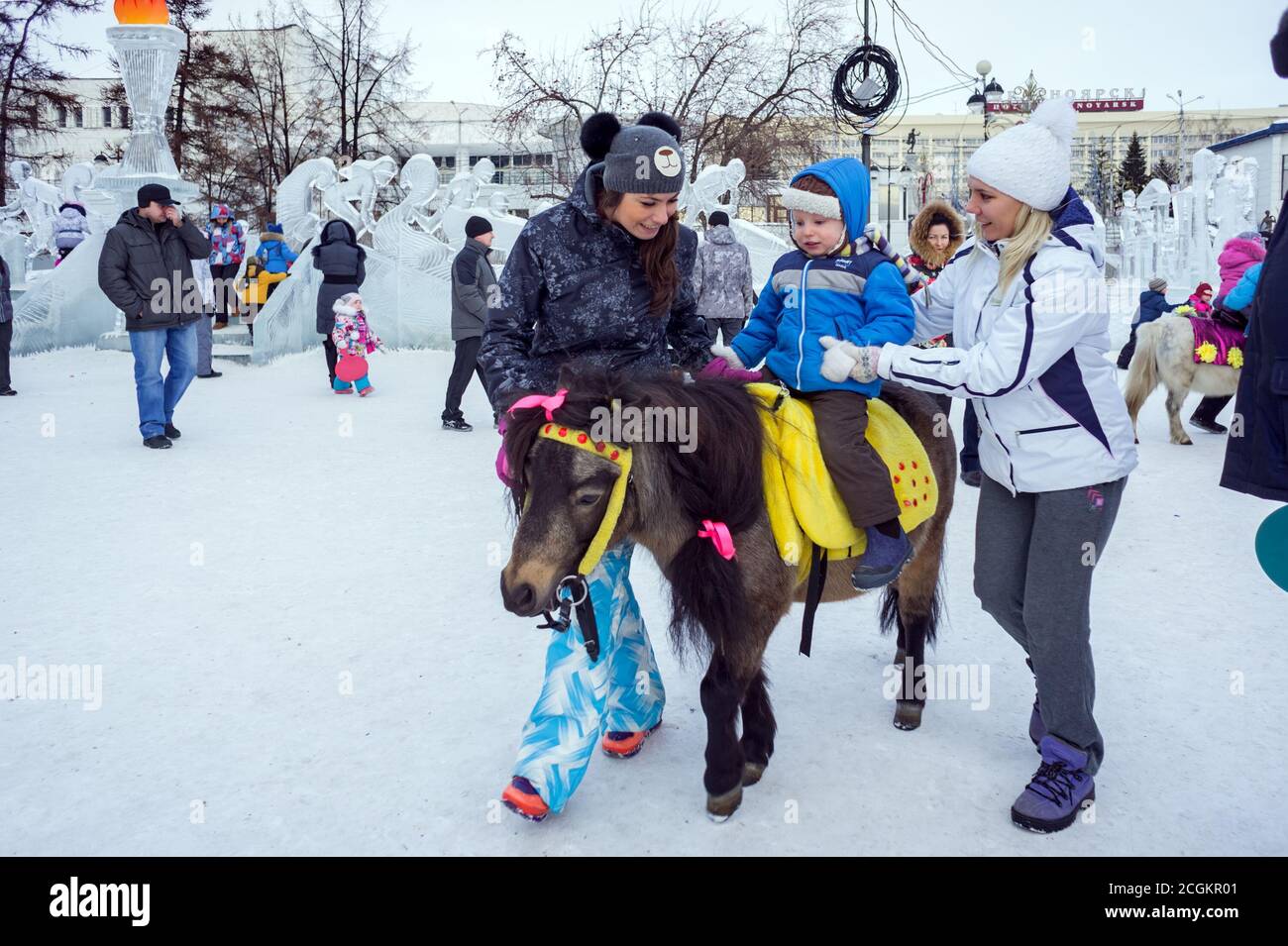 Un bambino sta cavalcando un pony intelligente sullo sfondo un parco di divertimenti sul ghiaccio nel centro di Krasnoyarsk durante le vacanze di Natale. Krasnoyarsk Territos Foto Stock