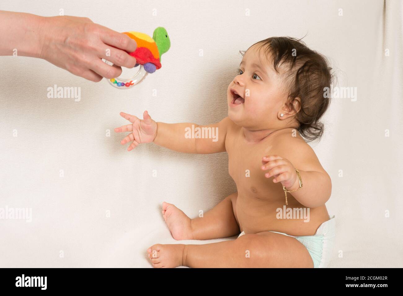 bambina di 6 mesi seduta, guardando il giocattolo penzolante, eccitato, interessato, cominciando a raggiungerlo Foto Stock
