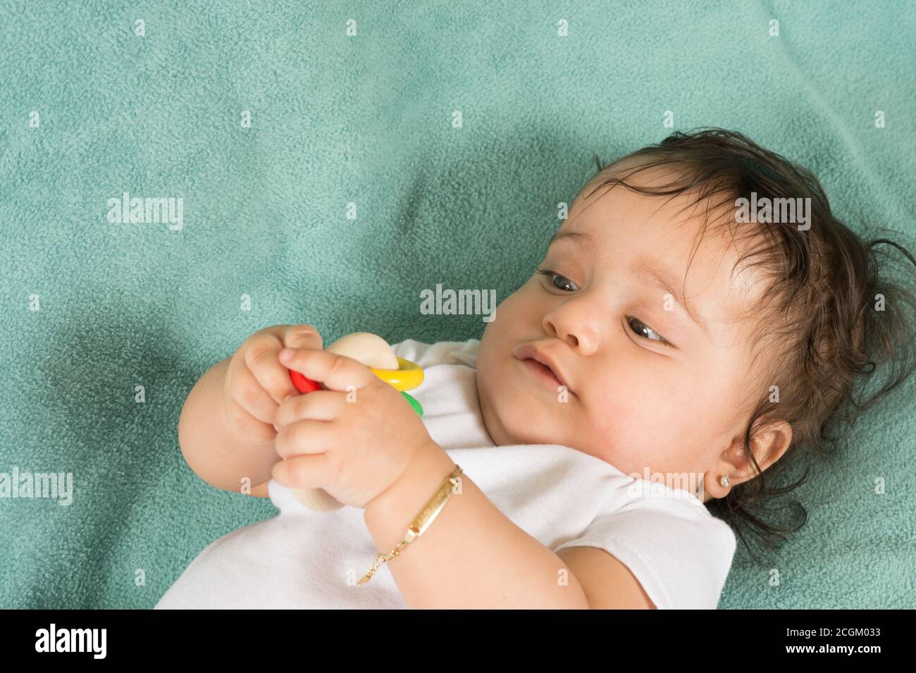 bambina di 6 mesi sulla schiena ravvicinato tenendo ed esaminare il sonaglino del giocattolo che sta tenendo con entrambe le mani Foto Stock