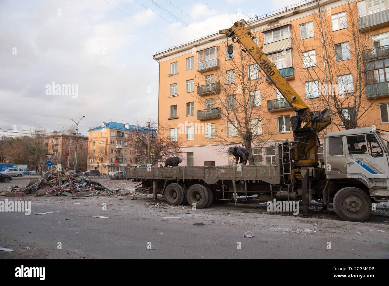 I lavoratori del servizio pubblico hanno messo i rifiuti di costruzione dalla demolizione di vecchi padiglioni in un camion con una gru su una strada cittadina. Foto Stock