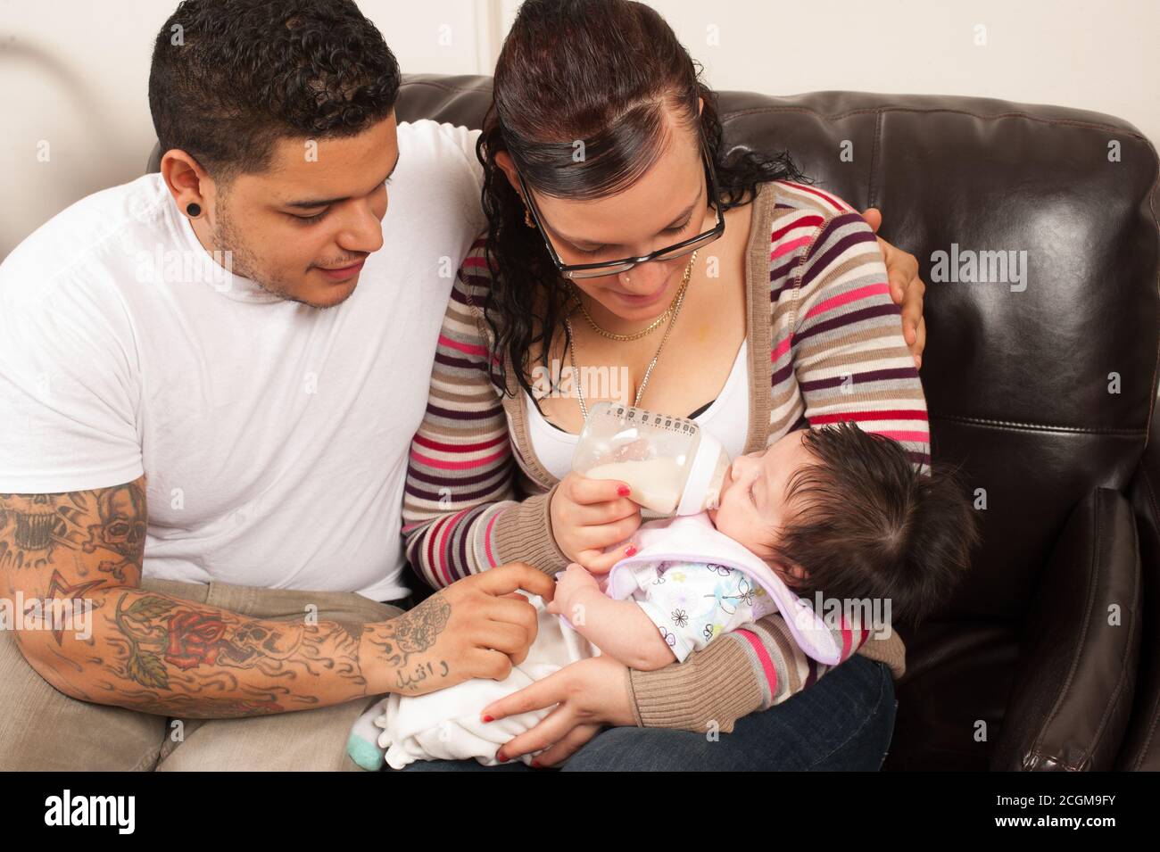 neonato bambina un mese con i genitori giovani, nutrendo la sua formula con un biberon, il padre ha tatuaggi sul braccio Foto Stock