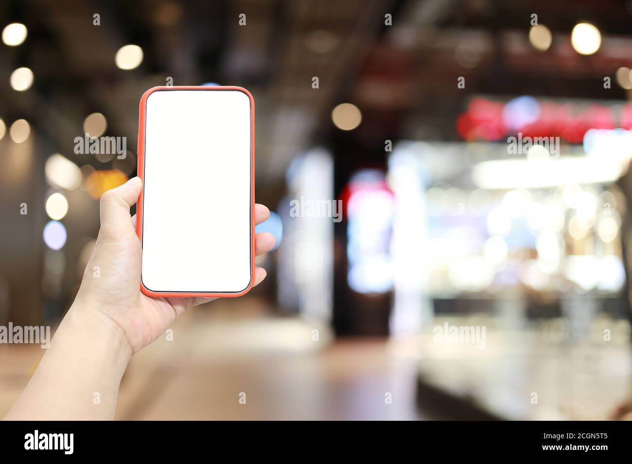 Mano di un uomo che tiene il dispositivo smartphone sullo sfondo del centro commerciale e che ha uno spazio di copia bianco sullo schermo. Foto Stock