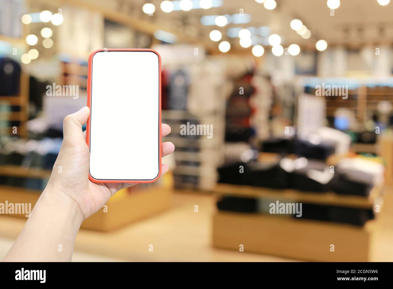 Mano di un uomo che tiene il dispositivo smartphone sullo sfondo del centro commerciale e che ha uno spazio di copia bianco sullo schermo. Foto Stock