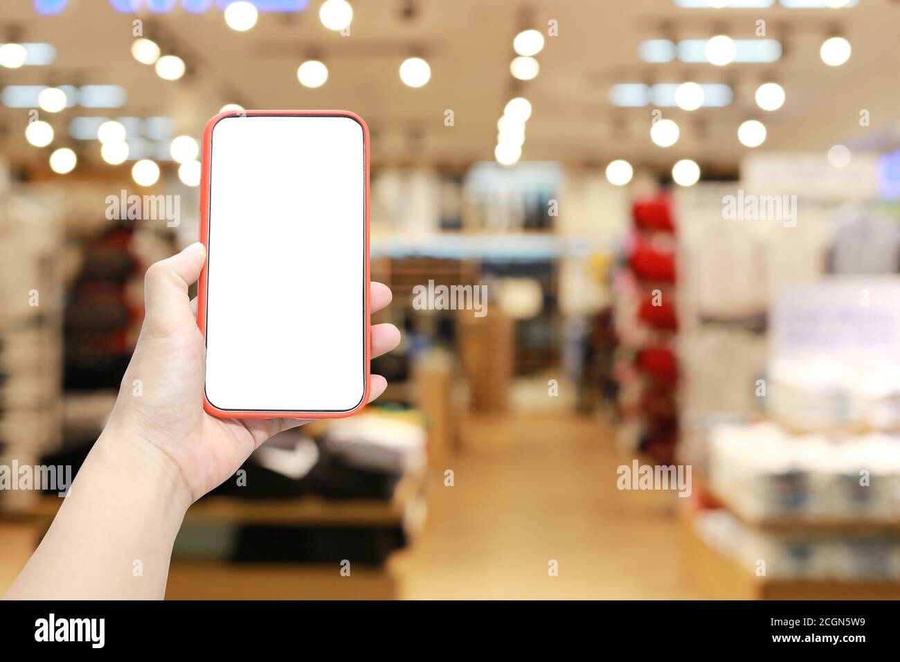 Mano di un uomo che tiene il dispositivo smartphone sullo sfondo del centro commerciale e che ha uno spazio di copia bianco sullo schermo. Foto Stock