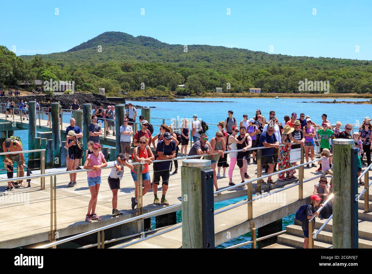 Isola di Rangitoto, Nuova Zelanda. Una folla di turisti aspetta un traghetto al molo. Sullo sfondo c'è il cono vulcanico dell'isola Foto Stock