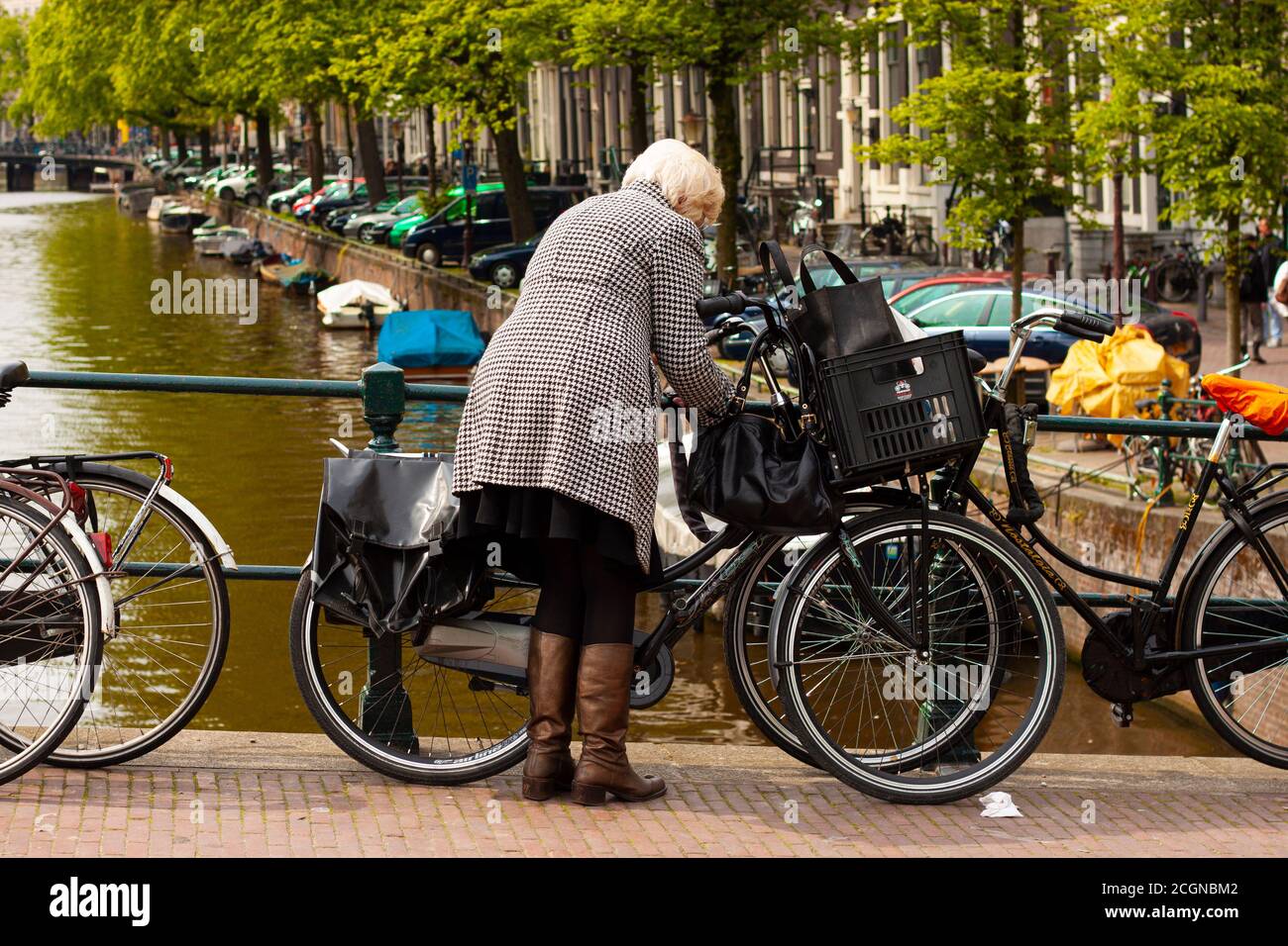 Amsterdam, Olanda 05/16/2010: Una donna anziana ben vestita che indossa stivali in pelle e un cappotto a scacchiera blocca la sua moto al raili Foto Stock