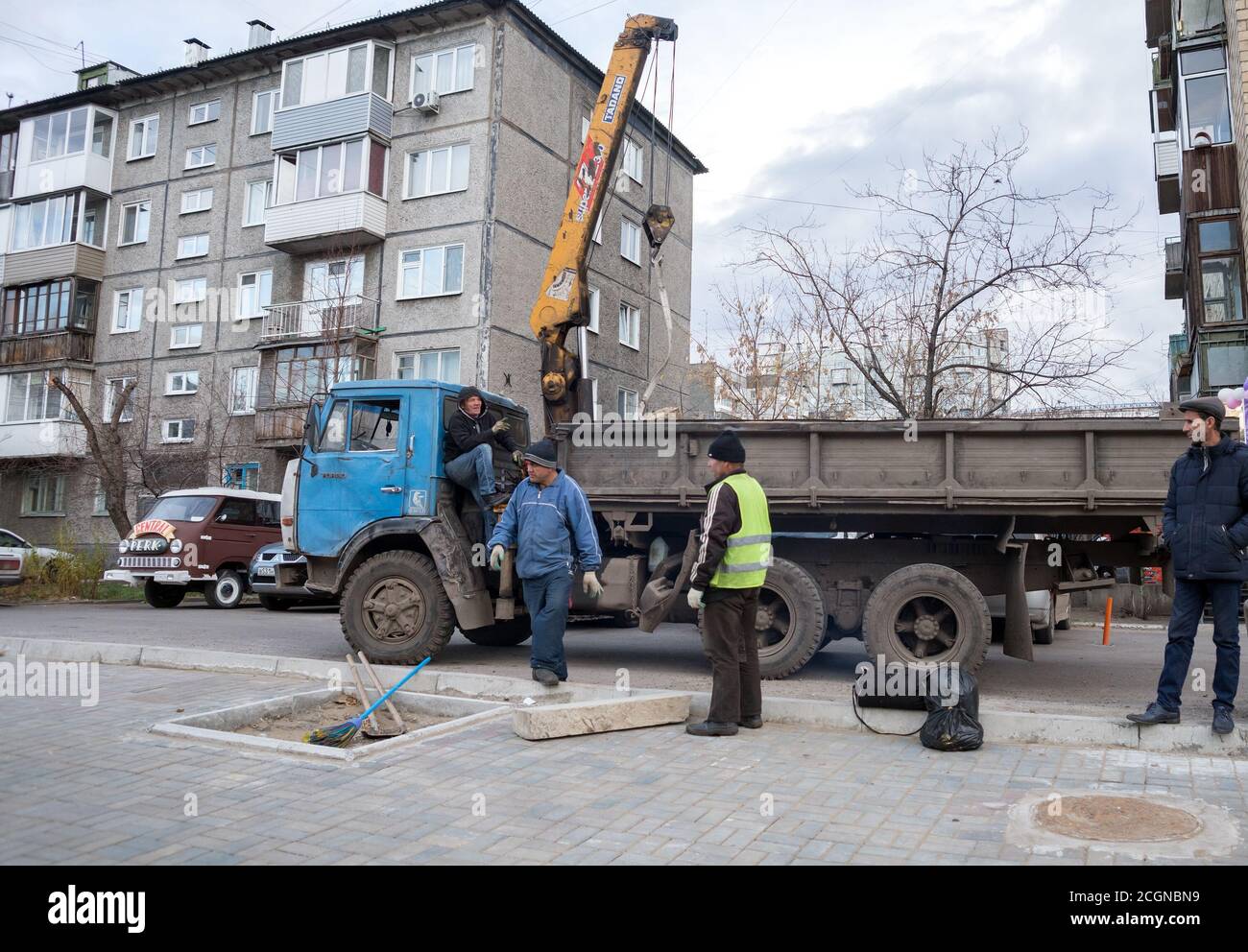 Verdi la città di Krasnoyarsk. I lavoratori sono impegnati a piantare un albero, portato da camion, in una zona residenziale sullo sfondo delle case. Foto Stock