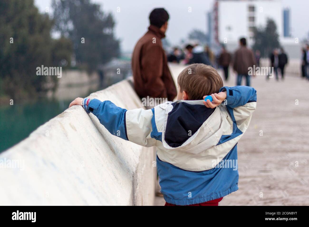 Un ragazzo sta gettando un tappo della bottiglia di plastica al fiume sopra le pareti di pietra di un ponte in un ambiente urbano. La mancanza di istruzione sembra essere responsabile di Foto Stock