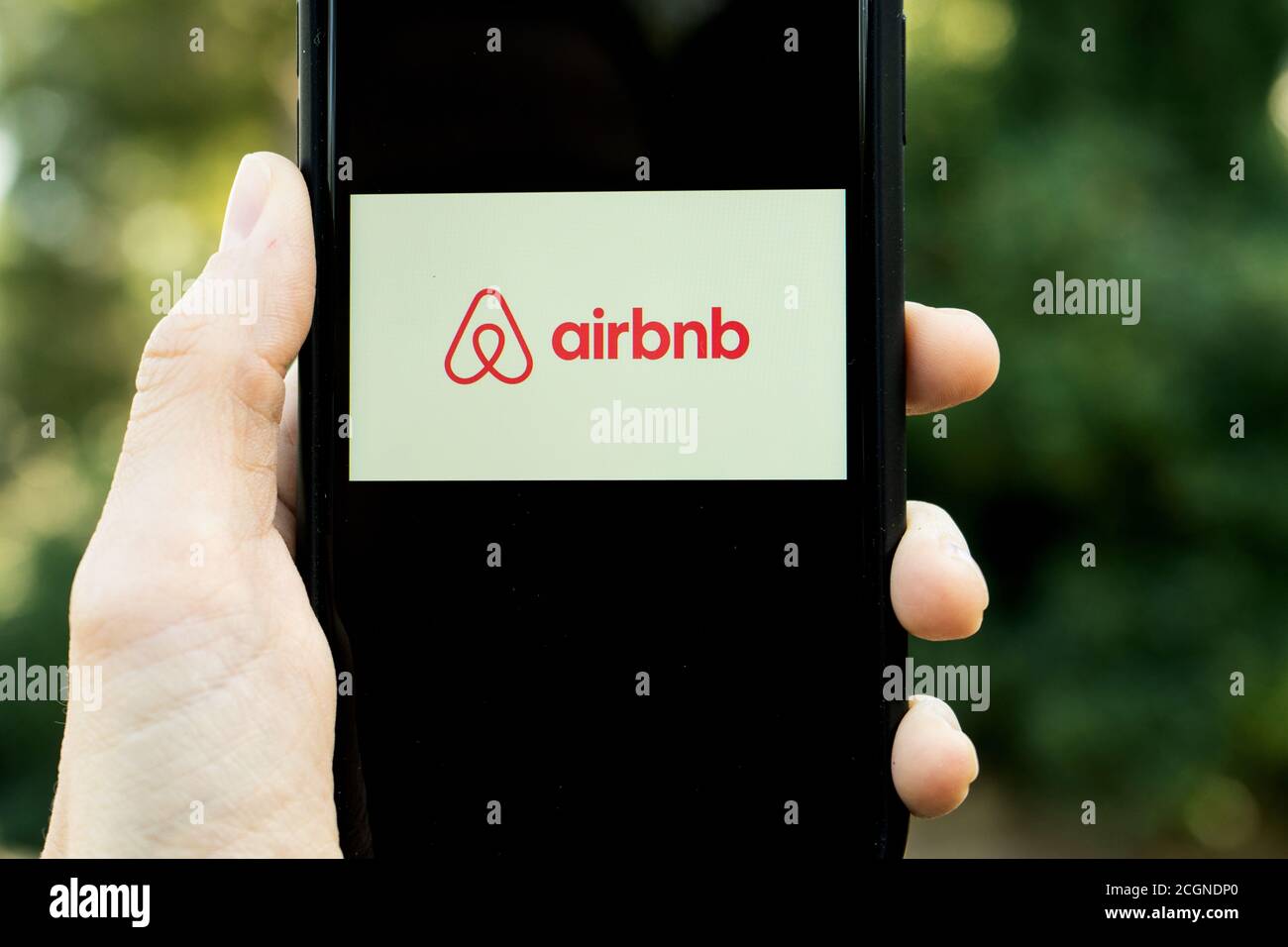 Mani che tengono iPhone 11 con un'app del servizio airbnb. Concetto di vacanza. Una donna che trova un posto dove soggiornare o prenotare un albergo, un appartamento Foto Stock