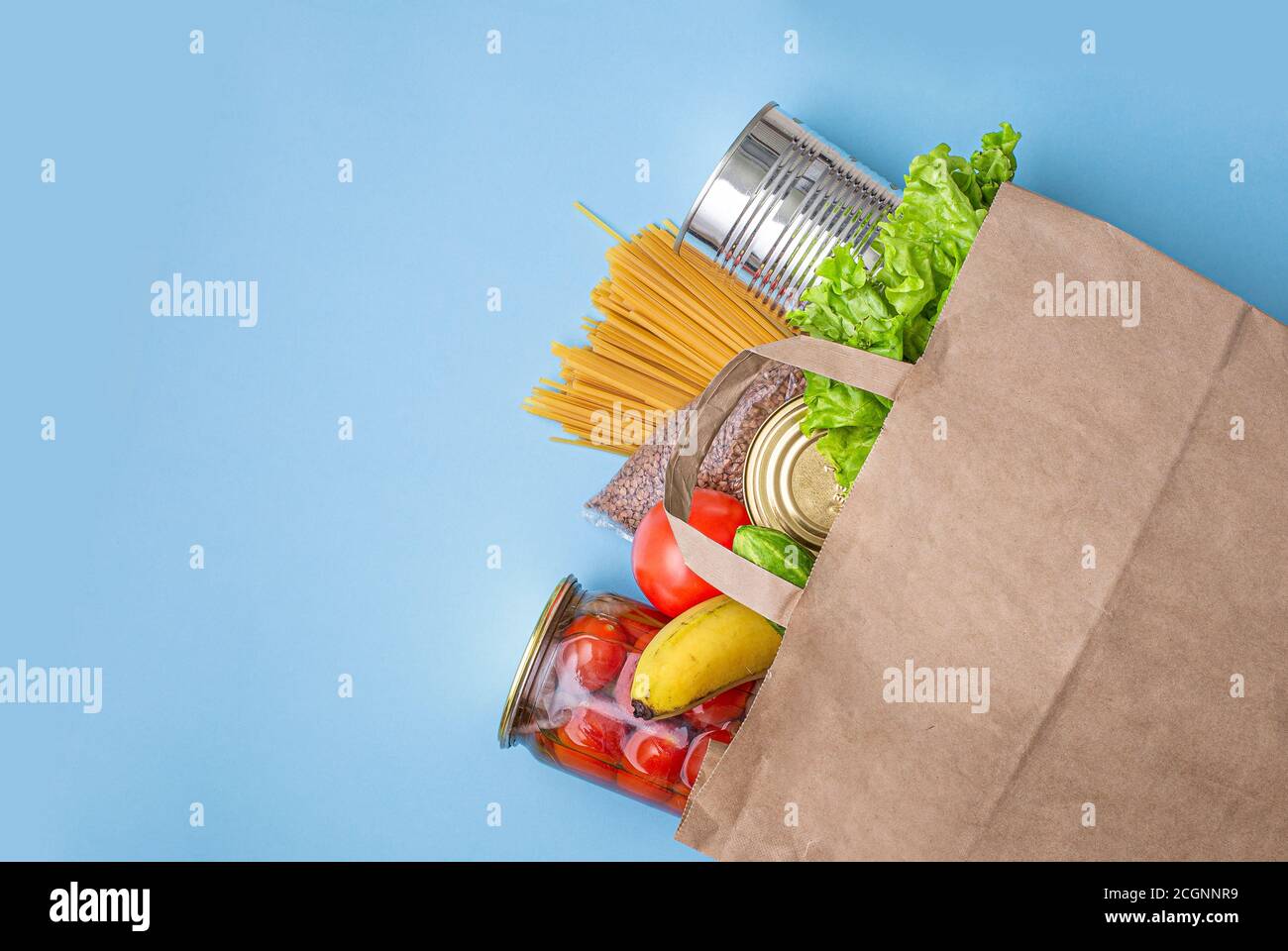 Sacchetto di carta con cibo, cibo in scatola, pomodori, cetrioli, banane su sfondo giallo. Donazione, quarantena coronavirus. Forniture alimentari per quarantena. Foto Stock
