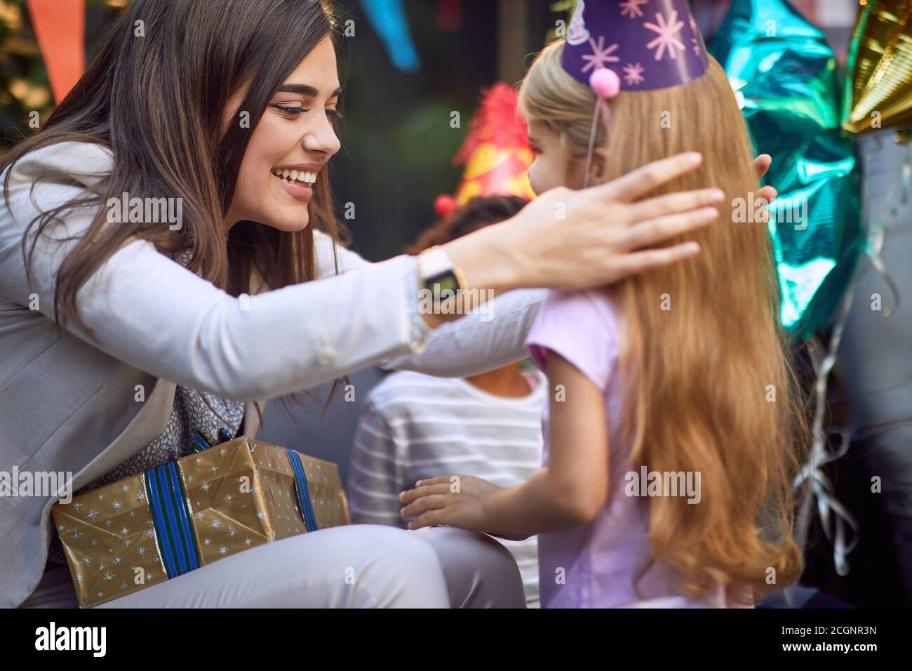giovane bella brunetta caucasica regolare i capelli ad un cute bambina bionda alla festa di compleanno Foto Stock
