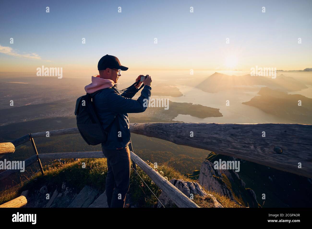 Giovane uomo che fotografa il paesaggio con il lago e le montagne all'alba. Vista dal Monte Pilatus, Lucerna, Svizzera Foto Stock