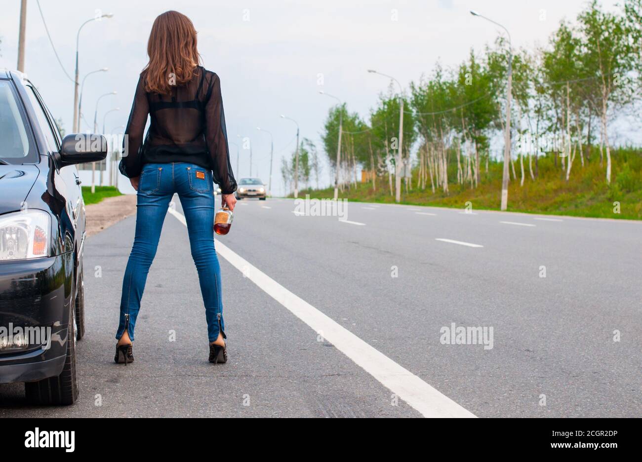 Una giovane donna si alza con cognac sulla strada successiva alla sua auto Foto Stock