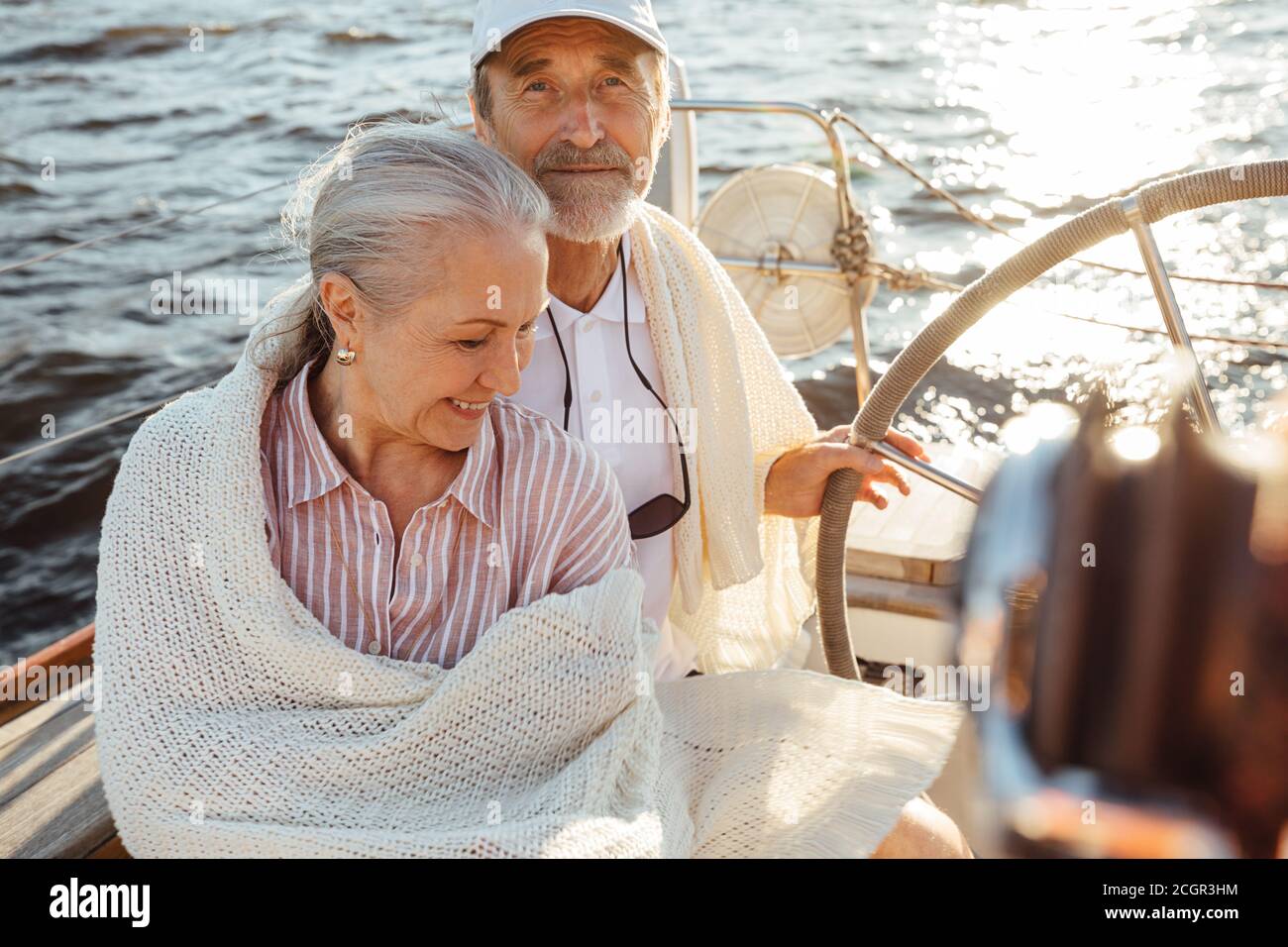 Un paio di due persone mature avvolte in plaid su una barca a vela. Uomo anziano in cappellotto che guida uno yacht. Foto Stock