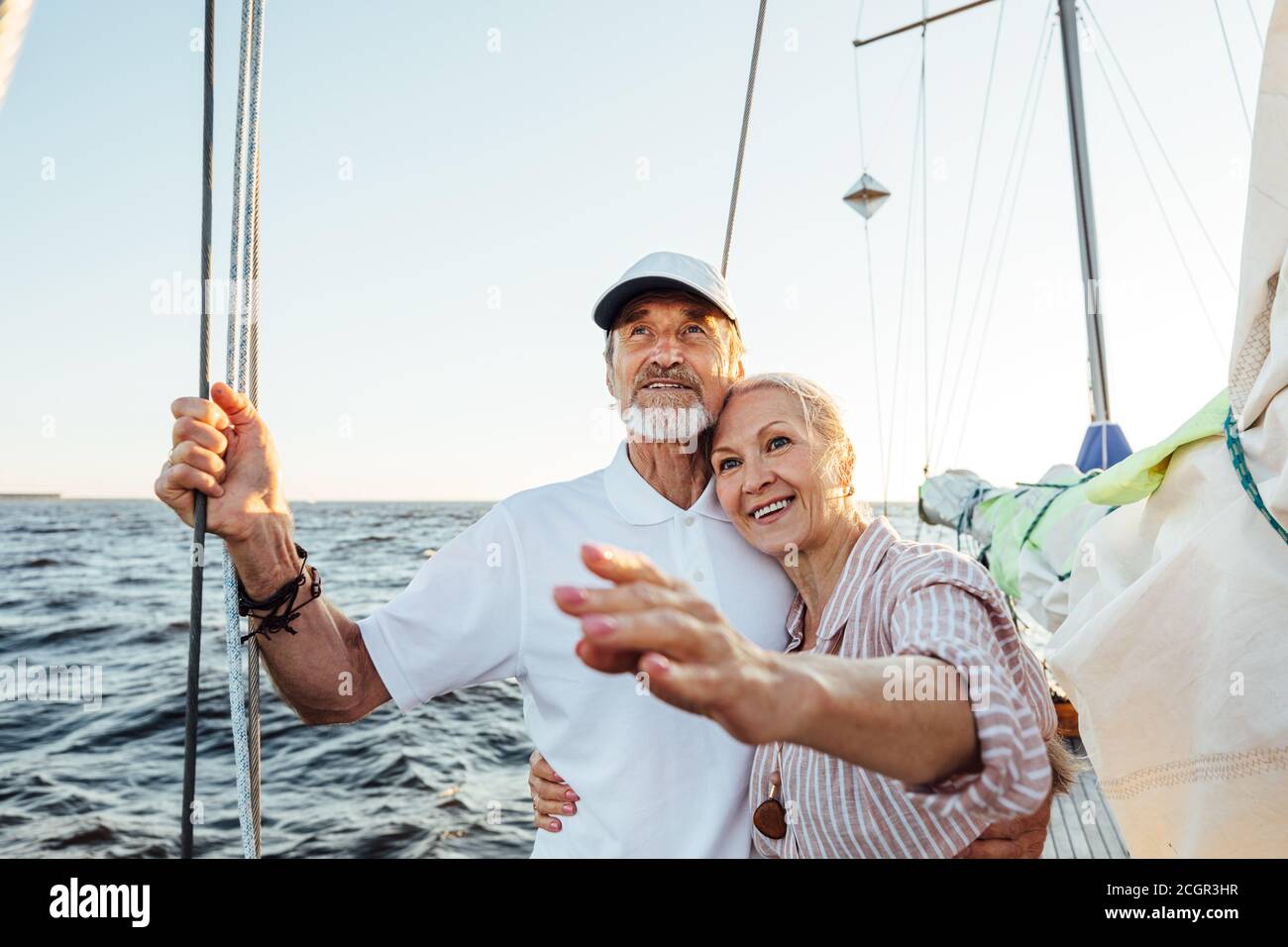 Felice donna matura che indica la distanza mentre abbracciando da suo marito sul loro yacht Foto Stock