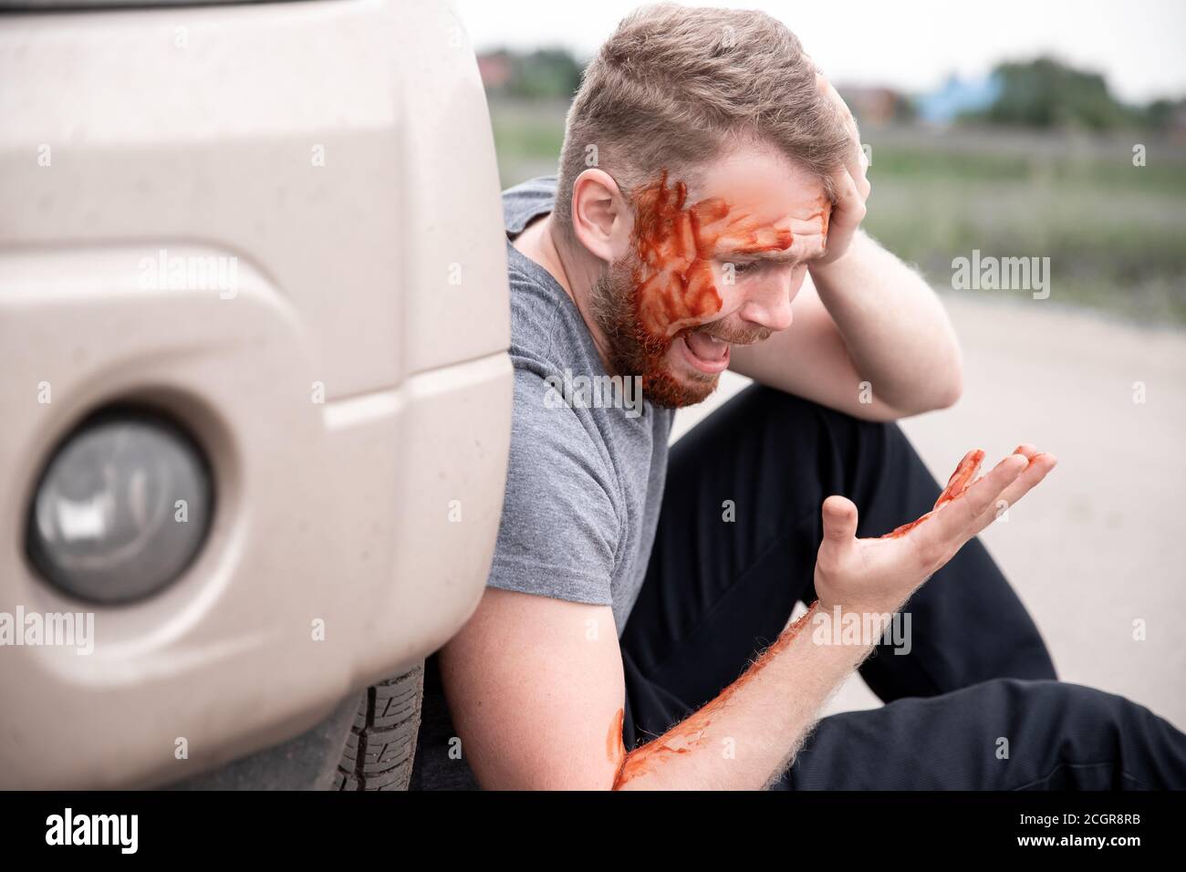 Il giovane si siede con la testa sanguinata vicino alla ruota dell'automobile, urlando e rammaricandosi atto Foto Stock