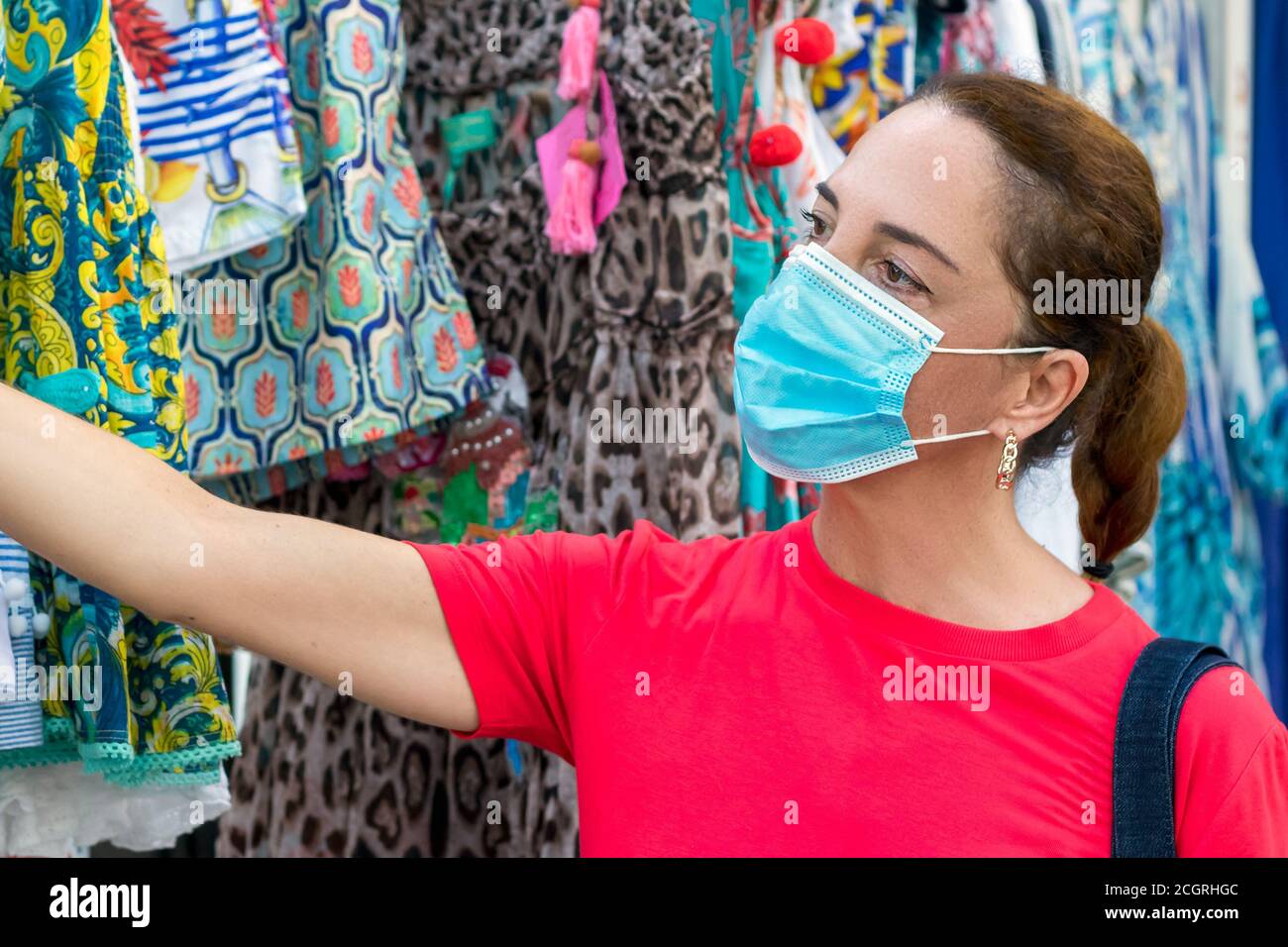 Donna matura che indossa maschera protettiva per il viso durante l'acquisto in un negozio di abbigliamento. Foto Stock