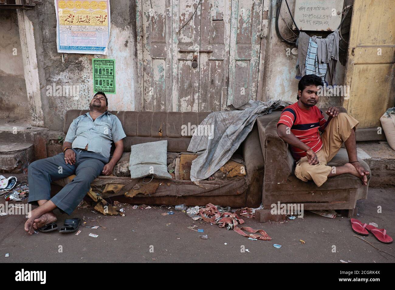 Due uomini in Rundown Arab Gully (Lane) nell'area di Grant Road, Mumbai, India, riposano rispettivamente su un vecchio divano scartato e consumato e su una poltrona Foto Stock