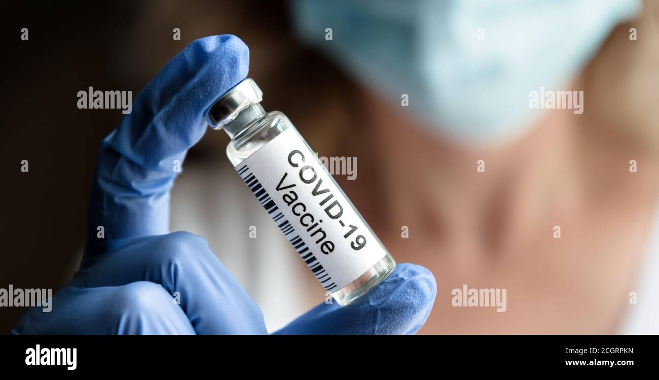 COVID-19 concetto di vaccino, il medico femminile tiene il farmaco del coronavirus in ufficio o in laboratorio. Flacone con vaccino per il trattamento del virus corona closeup. Foto Stock