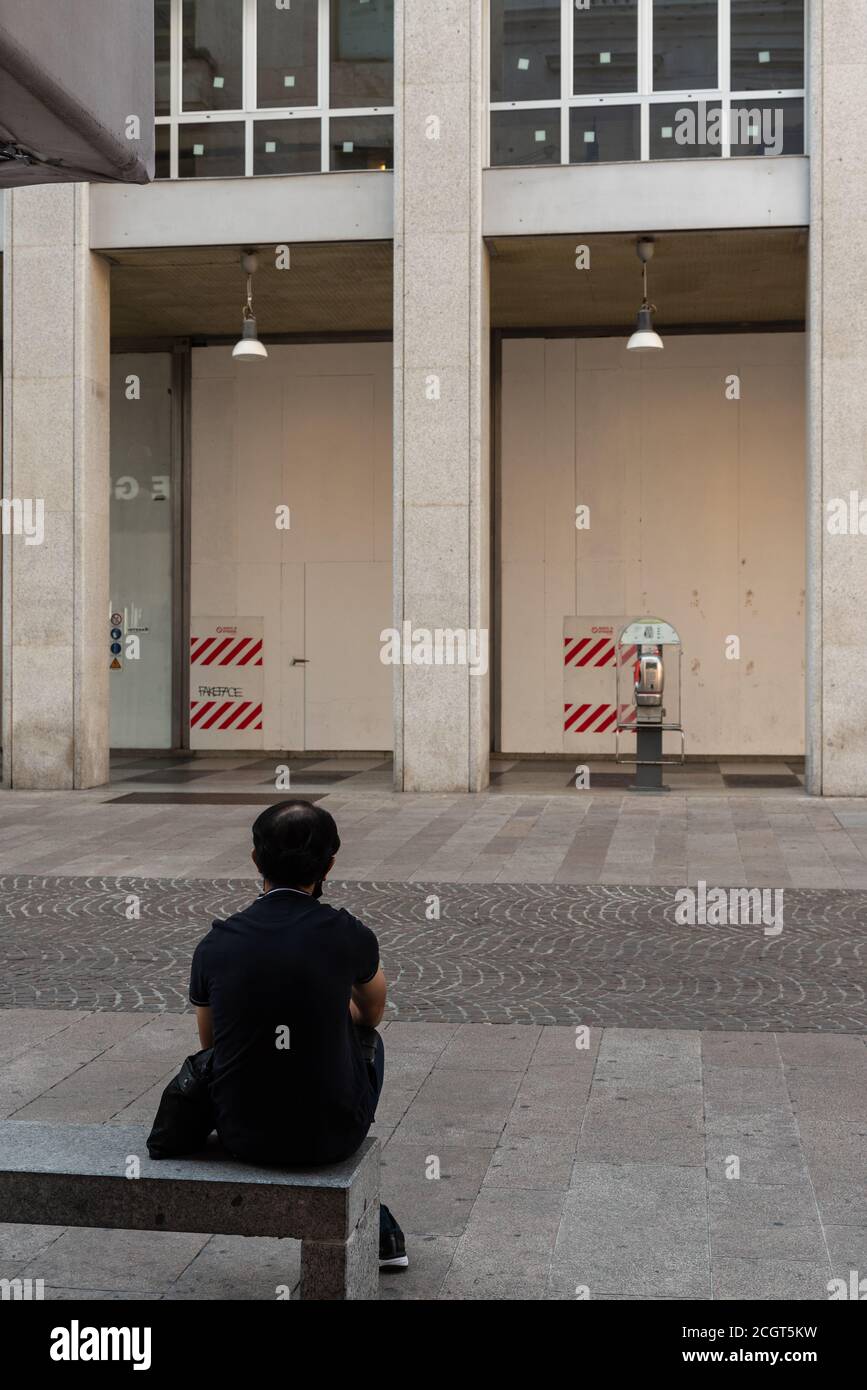 Uomo seduto su una panchina girata da dietro in una strada nel centro di Milano, fotografia di strada italiana Foto Stock