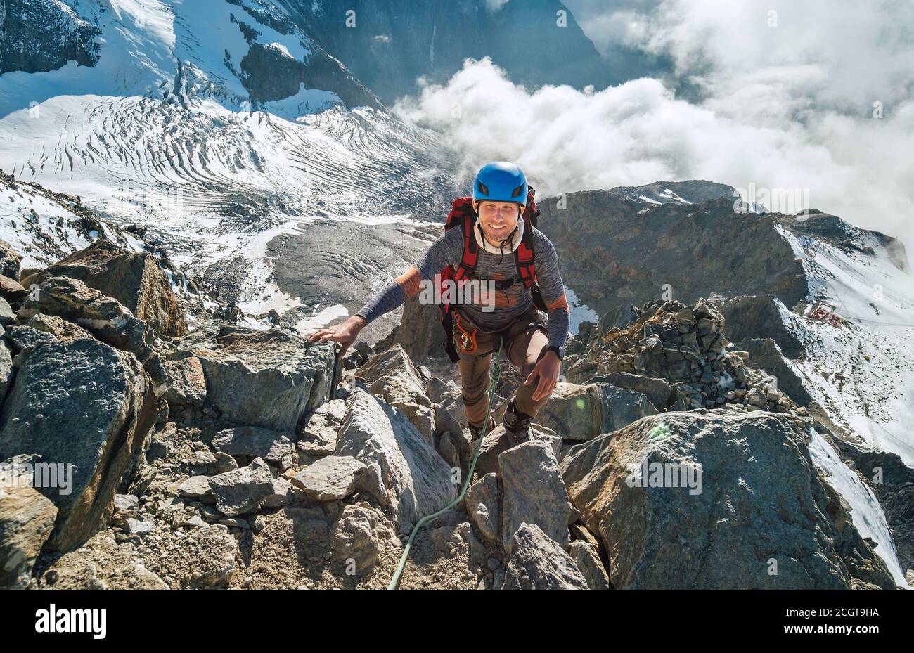 Arrampicarsi in un'imbracatura di sicurezza, casco con zaino salendo su una parete rocciosa con ghiacciaio Bionnassay sullo sfondo e guardando la cima durante il Monte Bianco A. Foto Stock