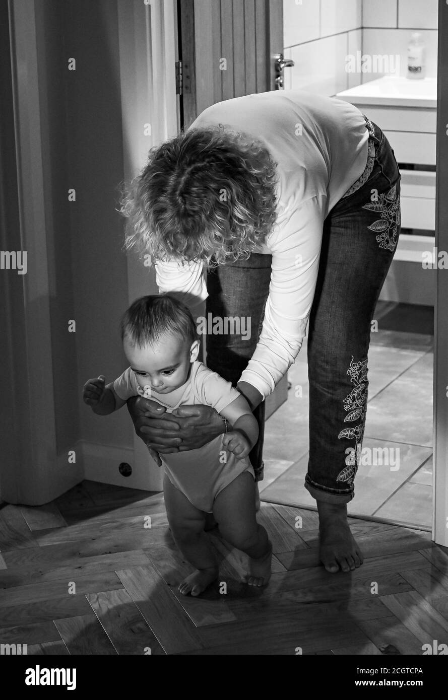 Bambino giovane di 10 mesi ragazzo imparando a camminare con sua nonna Foto Stock