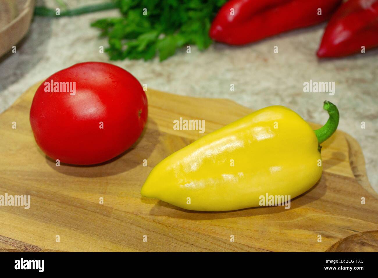 Pomodoro rosso, peperone giallo su tavola di legno. Prezzemolo, coriandolo e due peperoni rossi sul retro Foto Stock