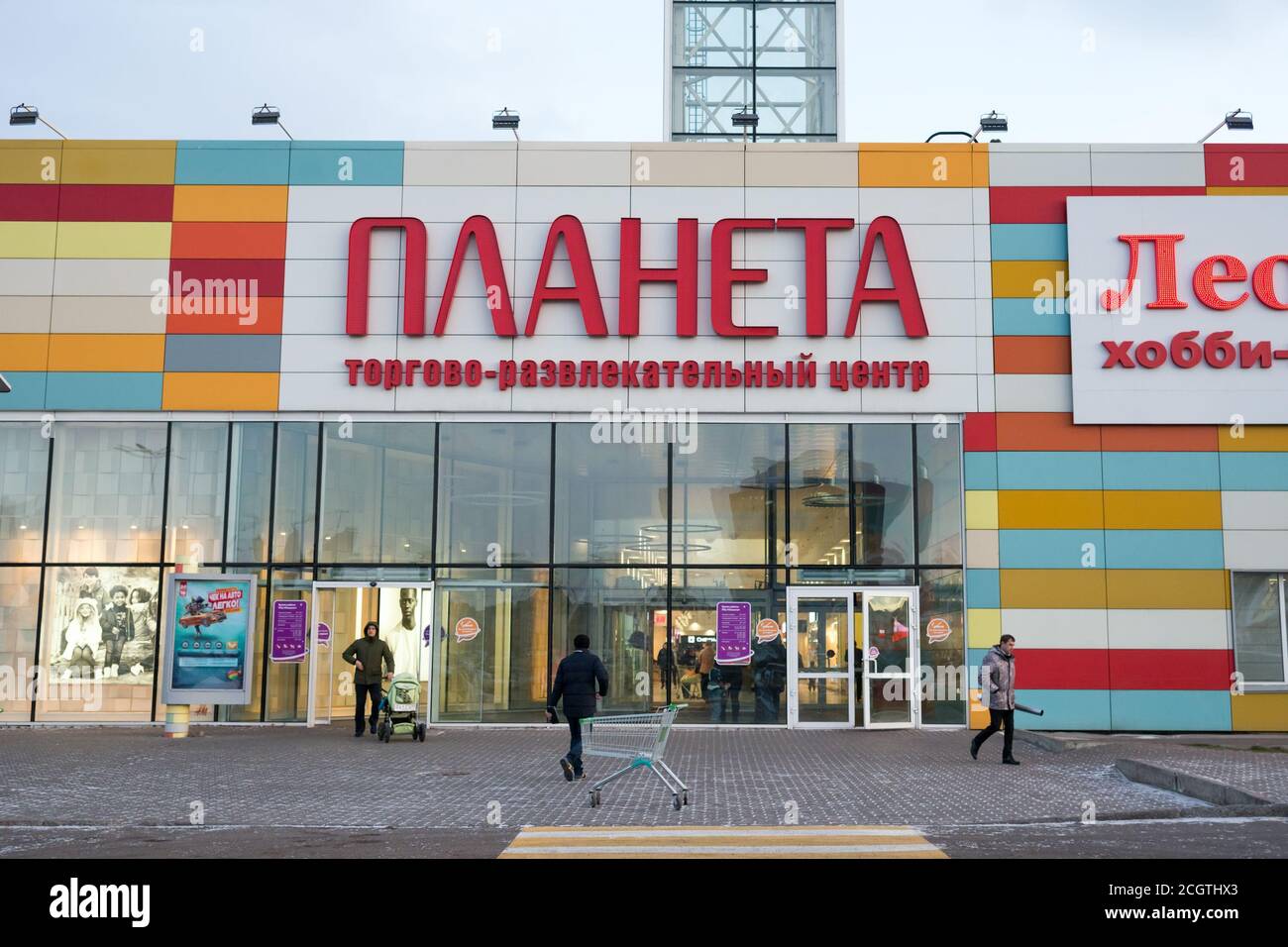 La gente viene e va al supermercato della città, con l'iscrizione in russo sul portico - Shopping e divertimento complesso Planet. Foto Stock