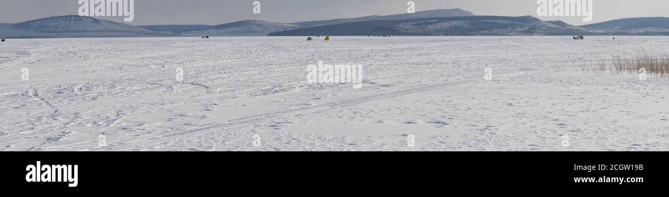 Paesaggio di un grande lago innevato stagnante con montagne all'orizzonte. Foto Stock