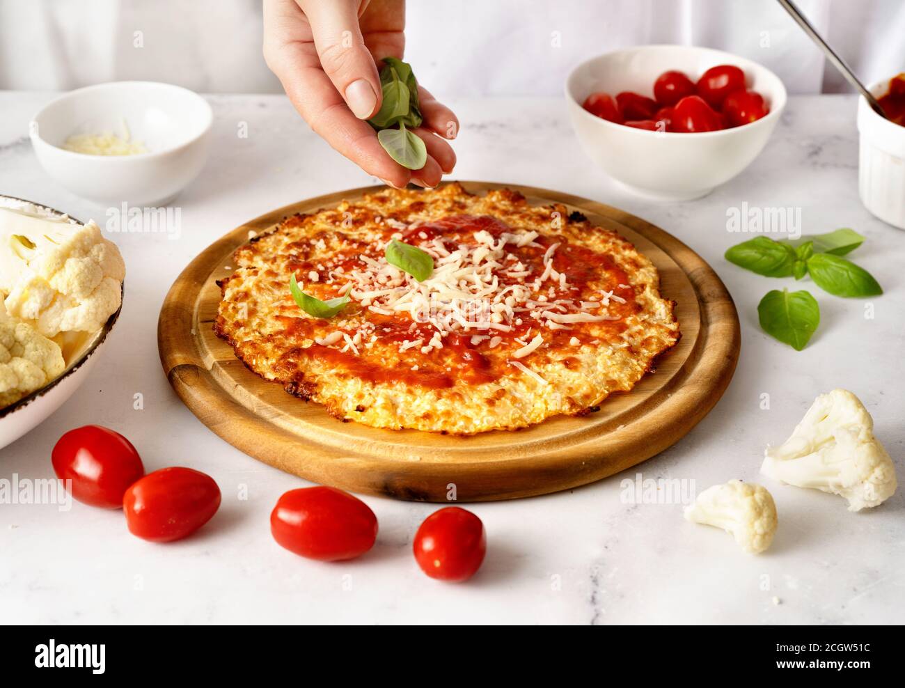 Le mani della donna spruzzano foglie di basilico fresco sulla parte superiore della crosta di pizza del cavolfiore. Keto dieta koncept. Cibo sano Foto Stock