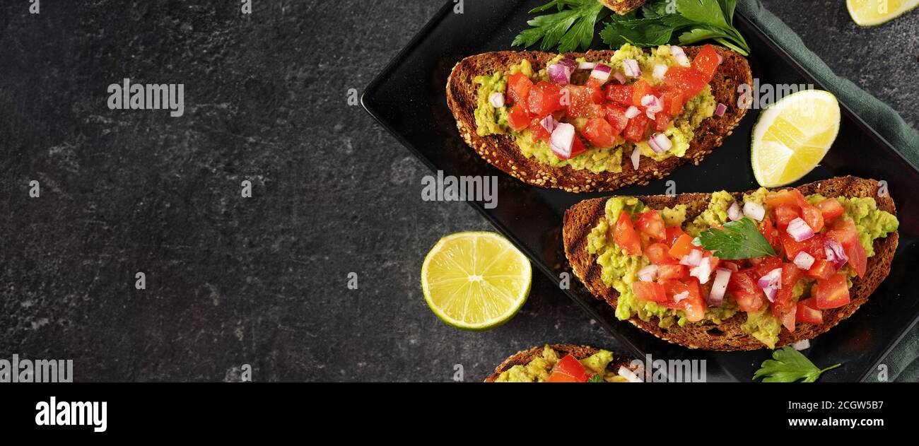 Primo piano di due sandwich di avocado vegano con pezzi di pomodoro su sfondo nero. Spazio di copia. Banner. Concetto di cibo vegano sano Foto Stock