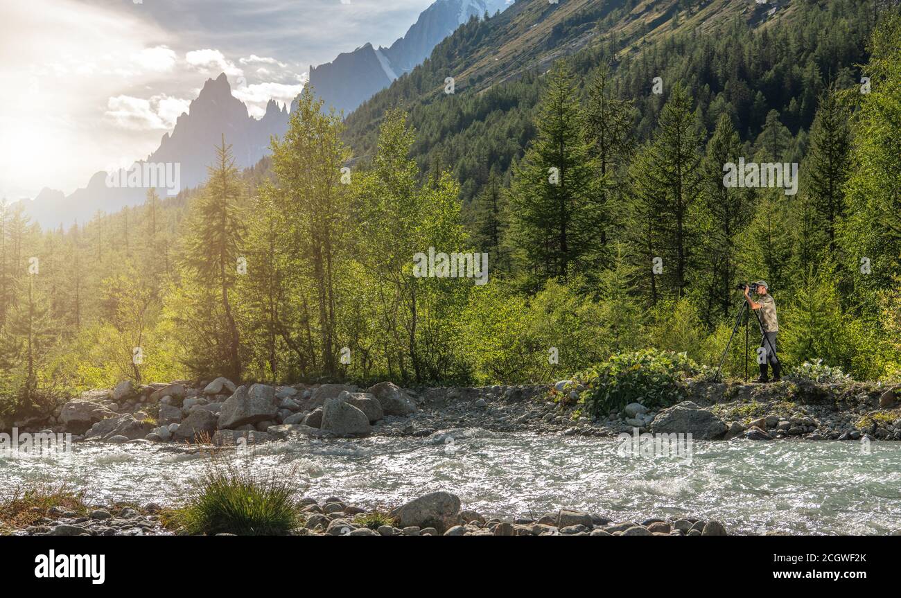 Fotografo naturalista come scattare foto utilizzando la fotocamera professionale accanto allo Scenic Mountain River. Paesaggio Alpino in background. Foto Stock