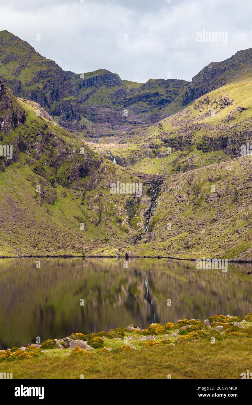 Vista attraverso una tranquilla crociera Loch verso la Corrie orientale e la Valle sotto Brandon Mountain sulla penisola di Dingle nella contea di Kerry, Irlanda Foto Stock