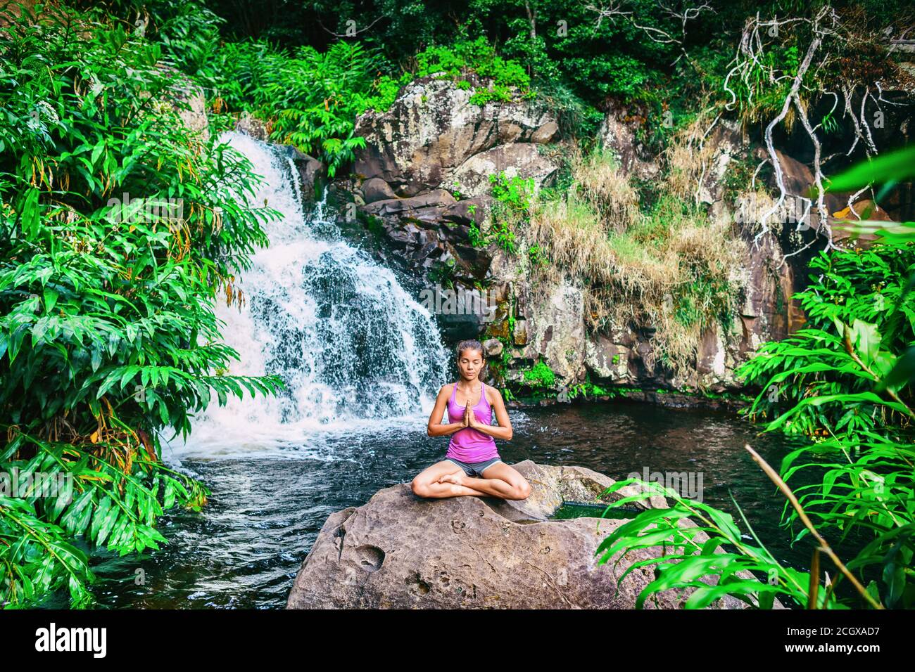 Yoga ritiro donna preghiera facendo il loto posa meditare a cascata foresta in Kauai, Hawaii. Ragazza spirituale che fa meditazione in serenità tranquilla Foto Stock