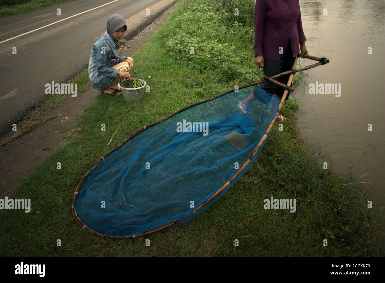 Una donna con un pushnet, preparatevi a pescare mentre si trova sulla riva di un canale di irrigazione nella reggenza di Karawang, provincia di Giava Occidentale, Indonesia. Foto Stock