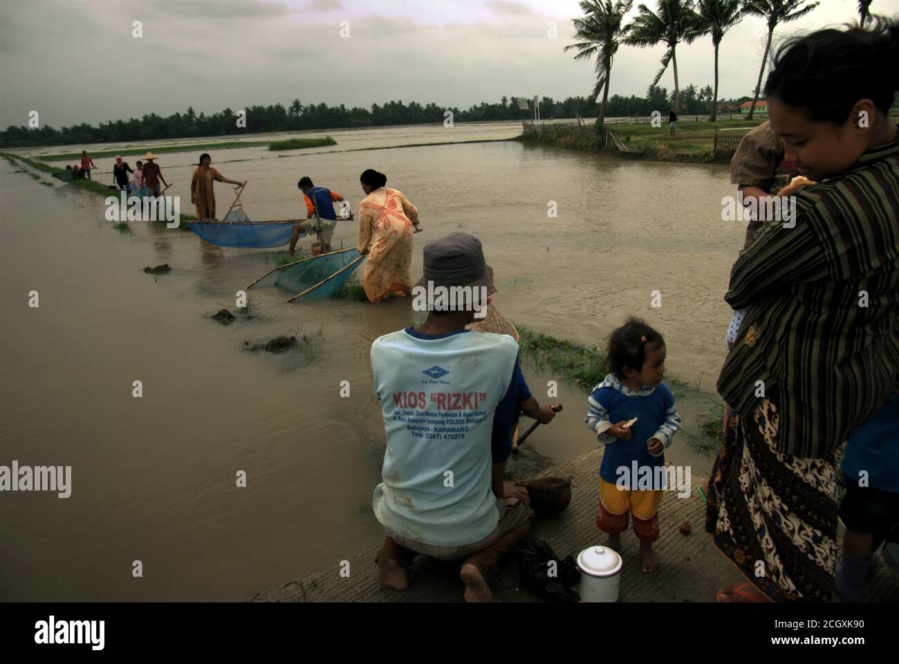 Gli agricoltori che pescano insieme da argini come piogge torrenziali durante la stagione delle piogge hanno lasciato alcune aree agricole allagate a Karawang, Indonesia. Foto Stock