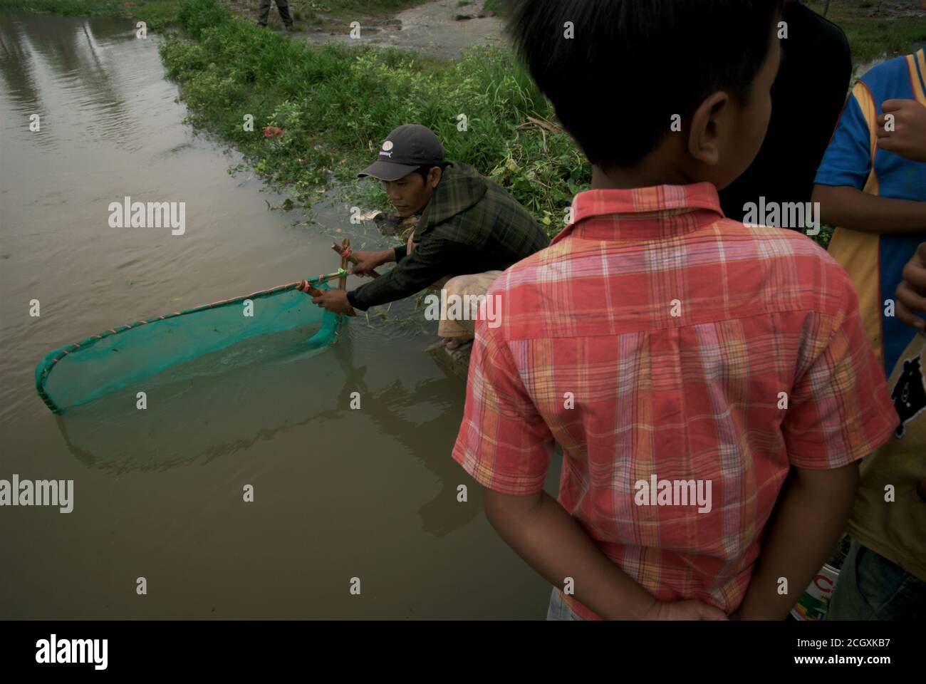 Un uomo che maneggia un pushnet, pesca sulla riva di un canale di irrigazione in Karawang regency, provincia di Giava Occidentale, Indonesia. Foto Stock