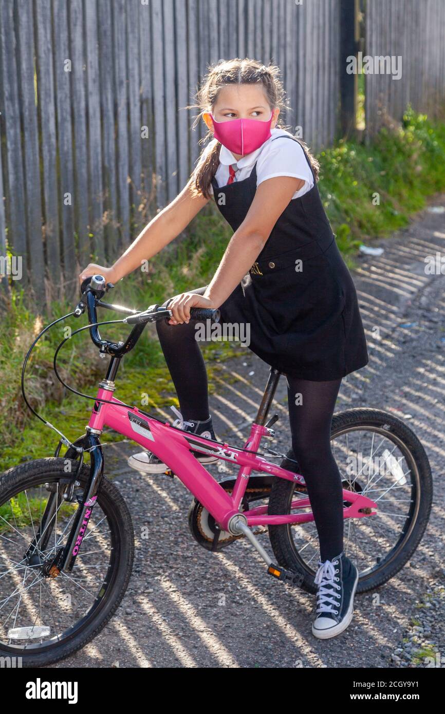 Una studentessa di dieci anni in uniforme da scuola seduta sulla sua bicicletta rosa e indossando una maschera rosa. Foto Stock