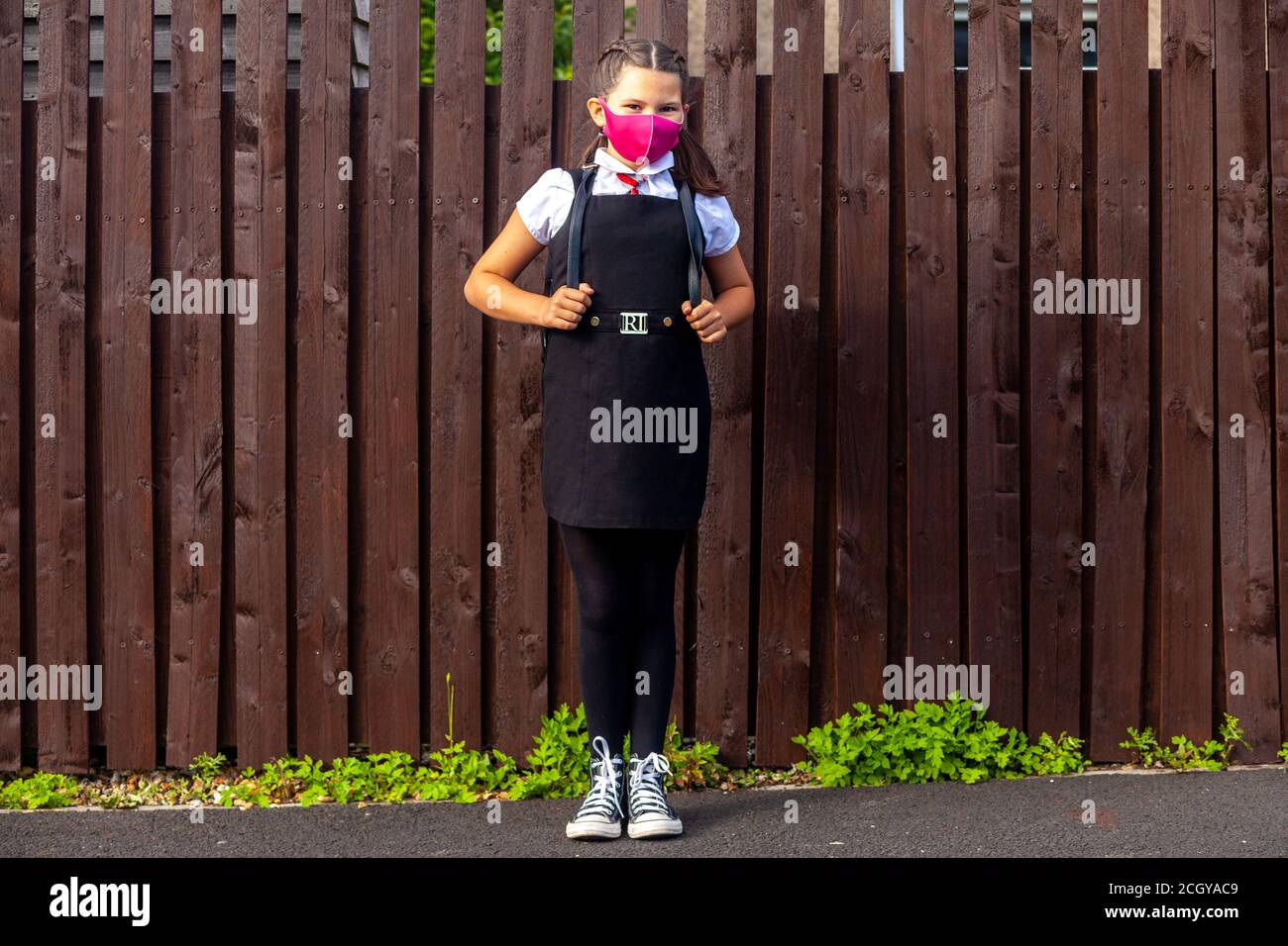 Una studentessa di 10 anni che indossa una divisa scolastica e una maschera rosa e guarda verso la macchina fotografica. Foto Stock