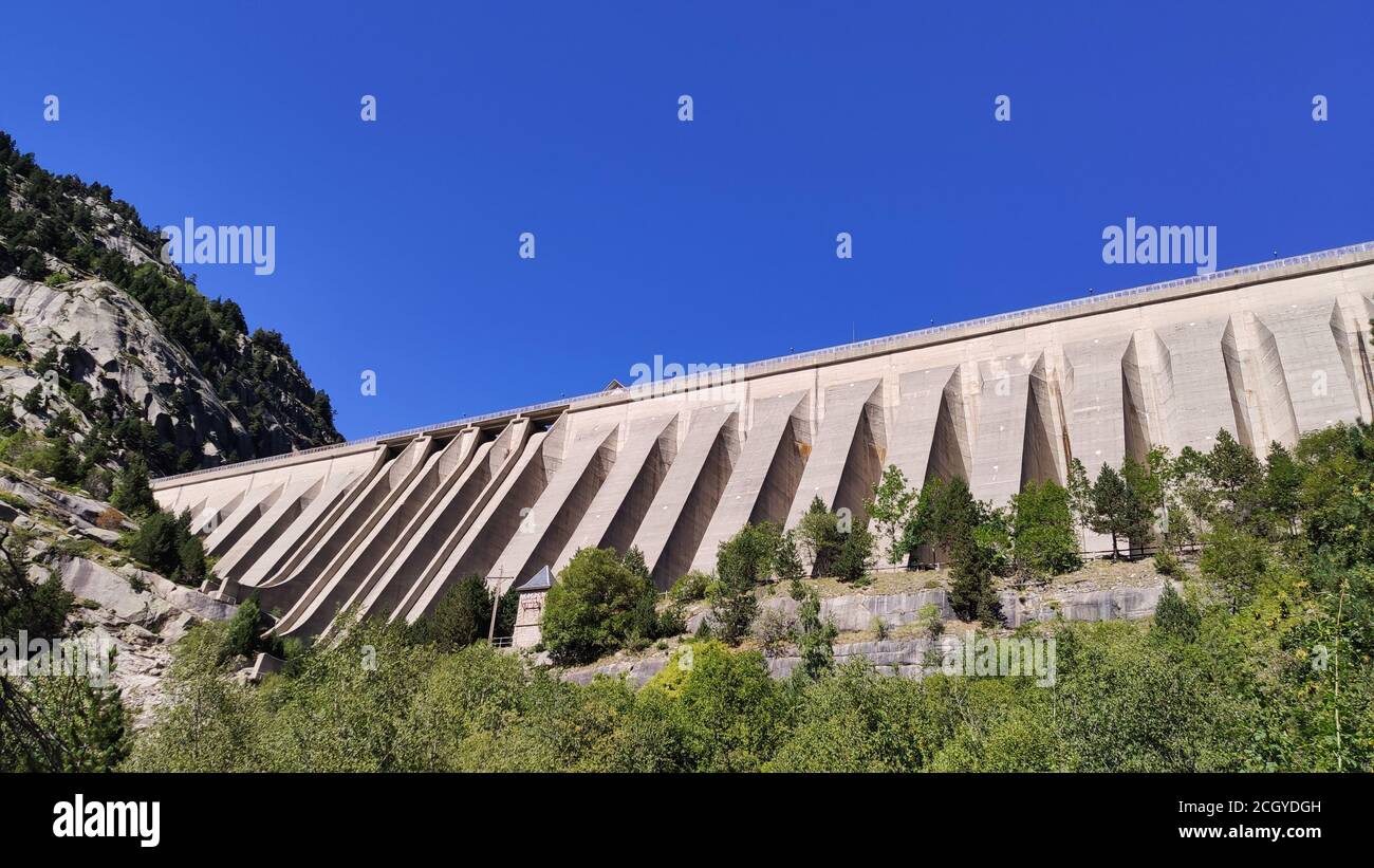 Foto di riserva della diga d'acqua vista dal basso, circondata da alberi sulla montagna Foto Stock