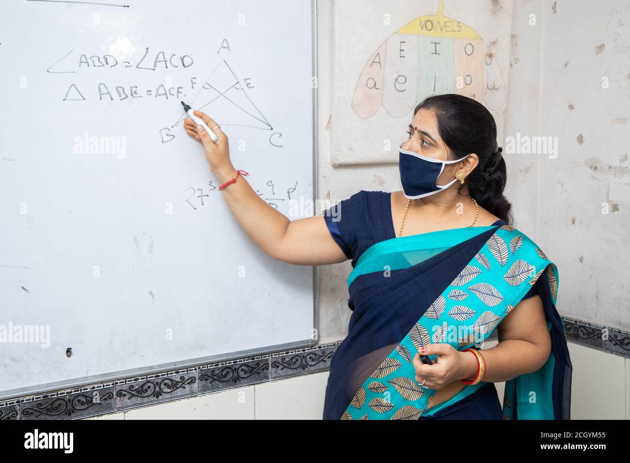 Insegnante femminile che indossa maschera e saree insegnano matematica su lavagna bianca in classe, scuola indiana classe di istruzione durante il cofid19 pandemia, nuova normalità Foto Stock